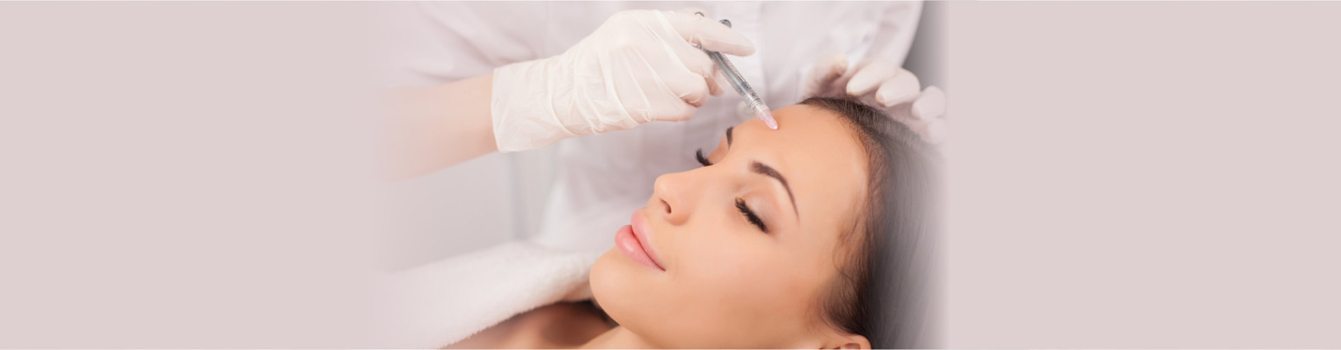 Close up of hands of expert beautician injecting botox in female forehead.